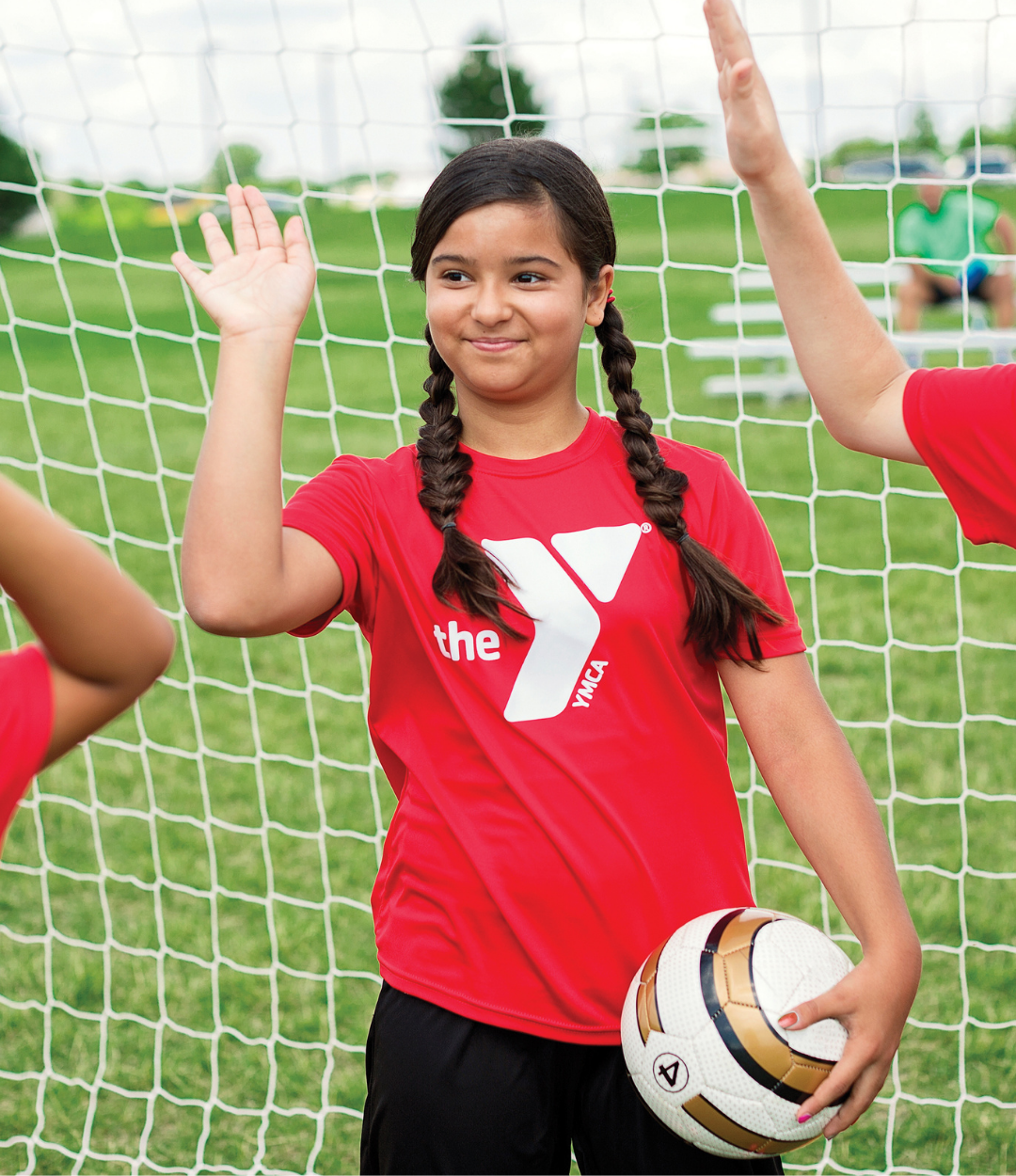 Boy and girls wearing Y shirts high five, one carrying a soccer ball.